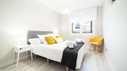 Un dormitorio blanco con una cama grande y una silla amarilla. en CAMBRILS BEACH 1a Línea Urbanizacion Playazul, en Cambrils