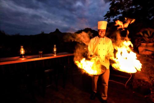 a chef walking on fire in front of a grill at Mantenga Lodge in Ezulwini