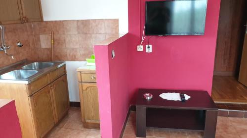 a pink kitchen with a table and a tv on a wall at Apartments Carevi Dvori in Jezera