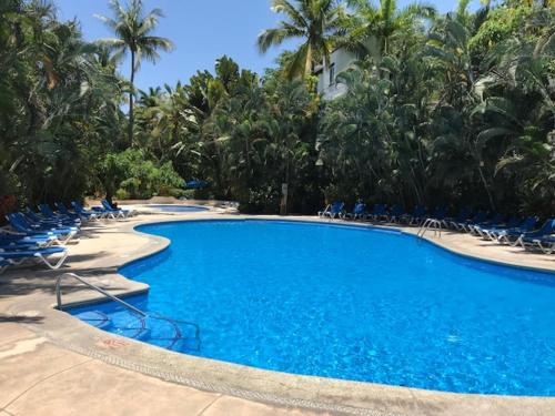 uma grande piscina azul com cadeiras e palmeiras em Hermoso departamento a una cuadra de la playa em Puerto Vallarta