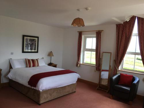 a bedroom with a bed and a chair and windows at Roskeel House in Achill