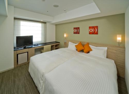 um quarto com uma grande cama branca e uma televisão de ecrã plano em Sotetsu Fresa Inn Yokohama Totsuka em Yokohama