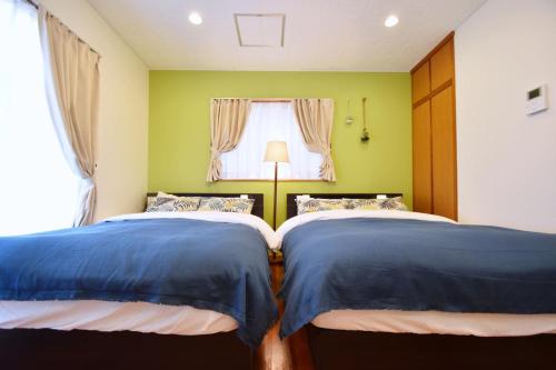 two beds in a bedroom with a window at Guest House Tsukishiro in Nanjo