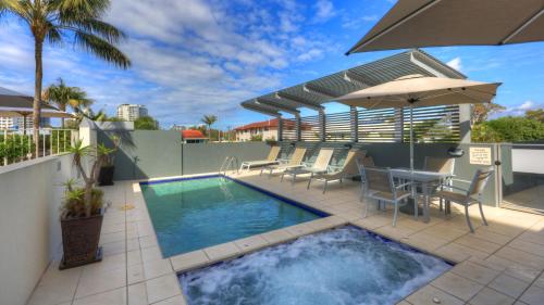 a swimming pool on a patio with chairs and an umbrella at The Dunes Cotton Tree in Maroochydore