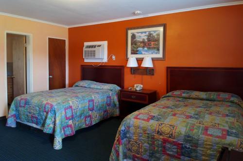2 łóżka w pokoju hotelowym z pomarańczowymi ścianami w obiekcie Encino Motel w mieście Pleasanton