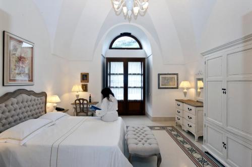 una donna seduta su un letto in una camera da letto di Resort Acropoli a Pantelleria
