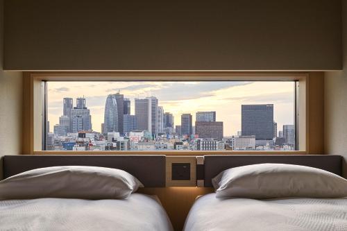 two beds in a hotel room with a view of a city at ONSEN RYOKAN YUEN SHINJUKU in Tokyo