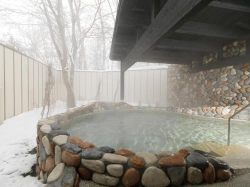 a hot tub with a stone wall in the snow at Hakodate Onuma Tsuruga Resort EPUY- 30km from Hakodate Station in Hakodate