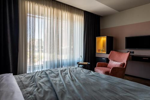 ein Hotelzimmer mit einem Bett, einem Stuhl und einem TV in der Unterkunft Maestro Design Hotel in Liepāja