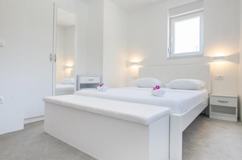a white bedroom with two beds and a window at Apartments Latkovic in Zaostrog