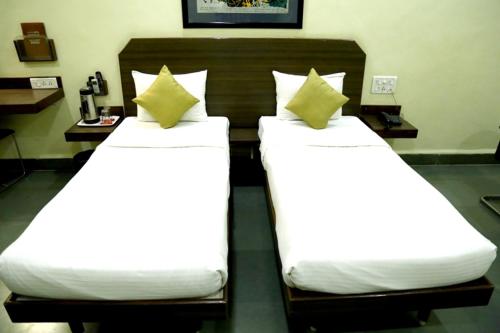 two beds with white sheets and yellow pillows in a room at Hotel Hospice in Surat