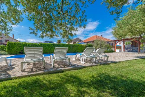 a group of chairs sitting in the grass near a pool at Apartments Coronata in Biograd na Moru