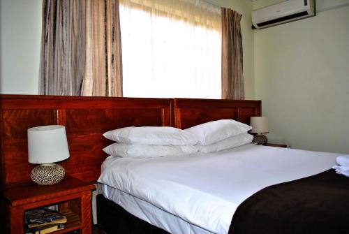 a bedroom with a bed with white sheets and a window at Mount Azimbo Lodge in Louis Trichardt