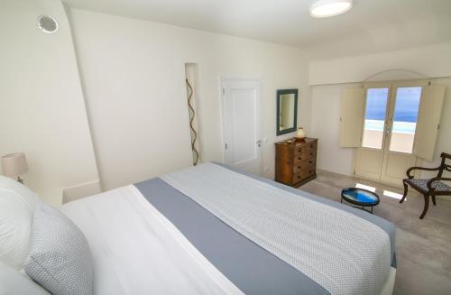 a white bedroom with a bed and a chair at Aloia Villas in Oia