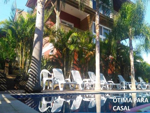 un groupe de chaises blanches et de palmiers près d'une piscine dans l'établissement Pousada Morro do Rosa, à Praia do Rosa