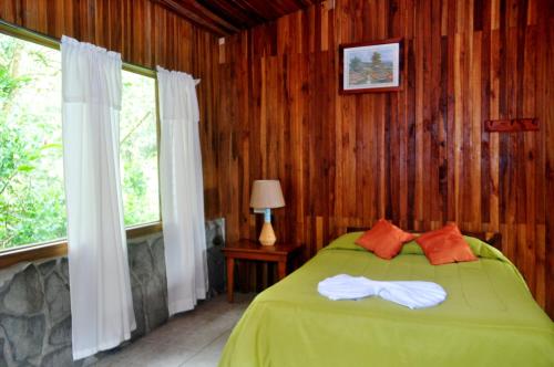 a bedroom with a green bed with wooden walls and windows at El Bosque Trails & Eco-Lodge in Monteverde Costa Rica
