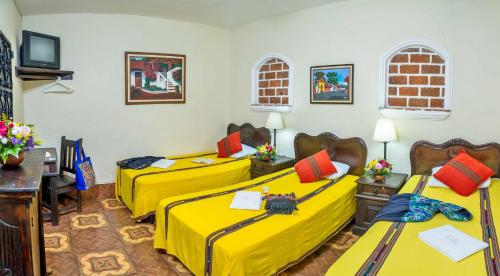 two beds in a room with yellow sheets at Posada San Vicente by AHS in Antigua Guatemala