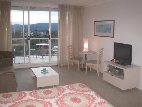 a living room with a bed and a television and a table at Ettalong Beach Luxury Apartments in Ettalong Beach