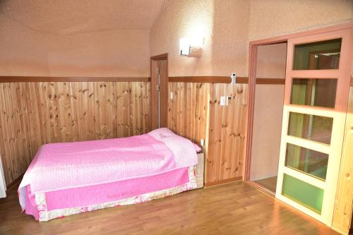 een slaapkamer met een roze bed en houten wanden bij Golmangtae Pension in Boseong