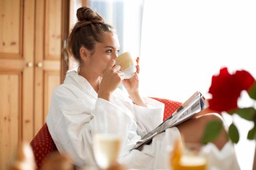 a woman sitting in a chair drinking a cup of coffee at Dolomiten Residenz - Sporthotel Sillian in Sillian