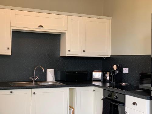 una cocina con armarios blancos y fregadero en Dovenby Apartment- great base for exploring Lake District, en Cockermouth