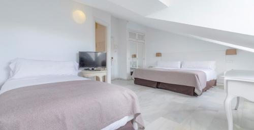 a white bedroom with two beds and a television at Hotel Suances in Suances