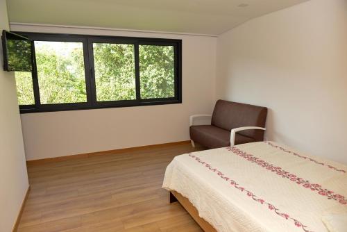 a bedroom with a bed and a chair and windows at Casa Encosta do Rio-ferias no Gerês in Vieira do Minho