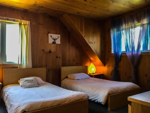 two beds in a room with wooden walls at Auberge Couleurs de France in Lac-Simon