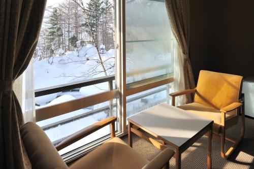 a room with a chair and a window with a view at Mogamitakayu Zenshichinoyu Ohira in Zao Onsen
