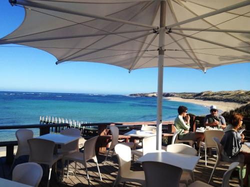 people sitting at tables under an umbrella on a beach at Margarets Beach Resort in Margaret River Town