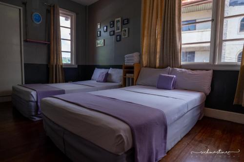 two beds in a room with two windows at Old Orangewood Bed & Breakfast in Baguio