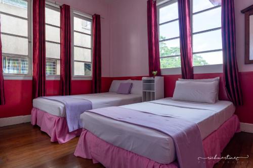 two beds in a room with red walls and windows at Old Orangewood Bed & Breakfast in Baguio