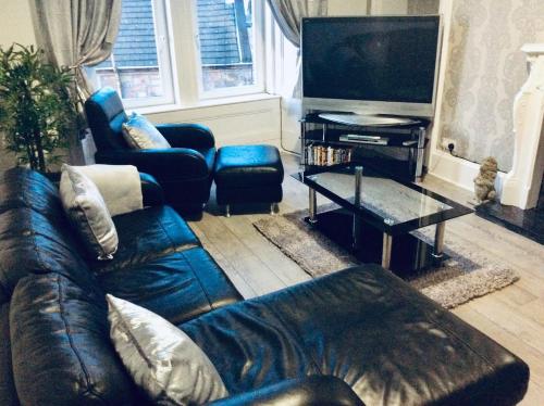 a living room with a leather couch and a television at THE LION'S DEN ON ROYAL STREET in Gourock