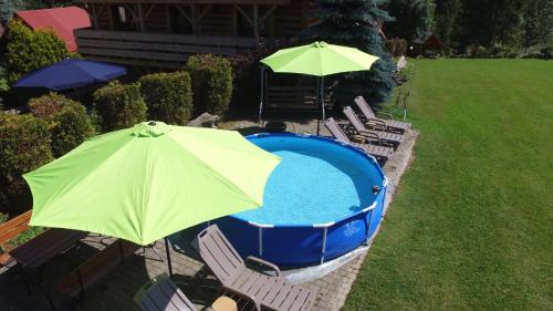 a pool with a green umbrella and chairs and a table at Ośrodek Wczasowy Wierchy in Korbielów