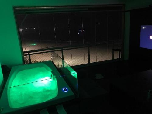 une chambre avec une télévision verte dans une pièce sombre dans l'établissement Maravilhoso Apto Vista Mar Jacuzzi Wi Fi Pé Areia, à Santos