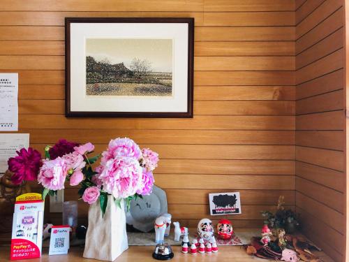 a table with pink flowers and a picture on a wall at 民宿とまとハウスTomato House in Funehiki