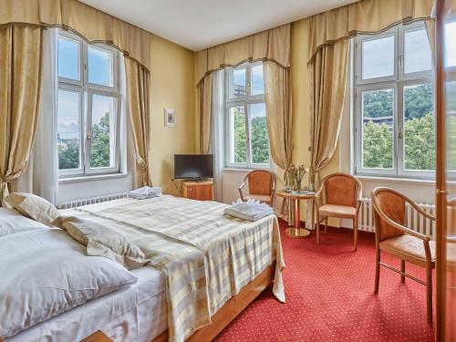 a bedroom with a bed and two chairs and windows at Hotel Sirius in Karlovy Vary