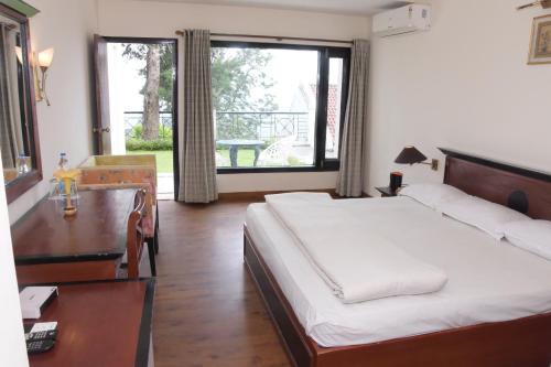 a bedroom with a bed and a desk and a window at The Pine Crest Resort Bhimtal in Bhīm Tāl