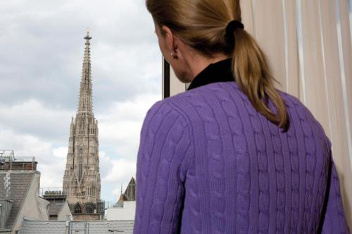 a woman in a purple sweater looking out a window at a cathedral at Appartement-Hotel an der Riemergasse in Vienna