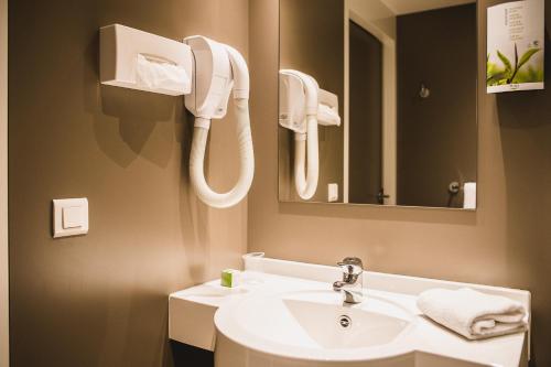 a white sink sitting under a mirror in a bathroom at DC Hotel & Restaurant Charleroi Airport in Charleroi
