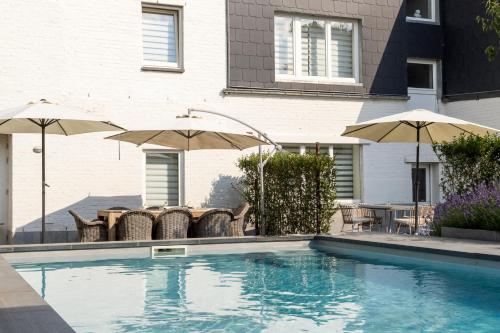 a swimming pool with chairs and umbrellas next to a house at B&B Hostellerie Marie in Eben-Emael