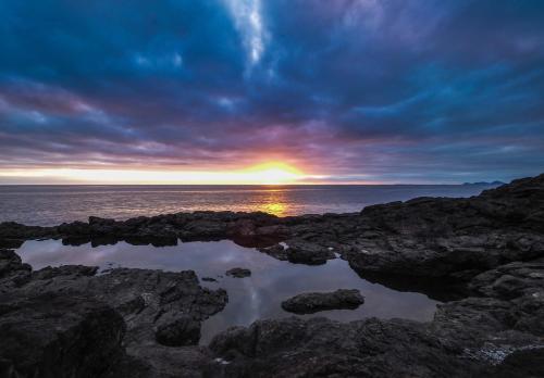 a sunset over a body of water with rocks at Te Whara at Kauri Mountain Point in Whangarei