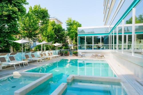 a swimming pool with chairs and a building at Aqua Hotel in Rimini
