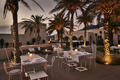 a restaurant with white tables and chairs and palm trees at Sikelia Luxury Hotel in Pantelleria
