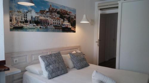 a white bed with two pillows and a painting on the wall at Hostal Ibiza in Ibiza Town