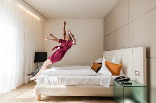 a woman jumping on a bed in a bedroom at Hotel Therme Meran - Terme Merano in Merano