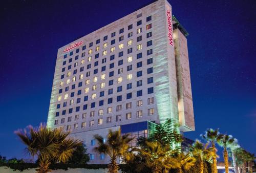 a tall building with palm trees in front of it at Mövenpick Hotel Amman in Amman