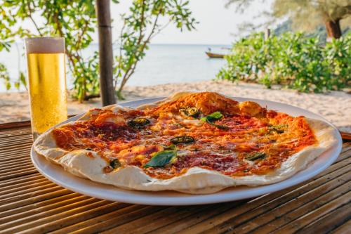 a pizza on a plate on a table with a glass of beer at SunBoo Beach Bungalows in Koh Rong Sanloem
