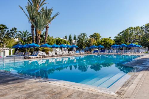 a swimming pool at a resort with chairs and umbrellas at Aliathon Aegean in Paphos City
