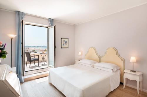 a white bedroom with a bed and a balcony at Hotel Sina Astor in Viareggio